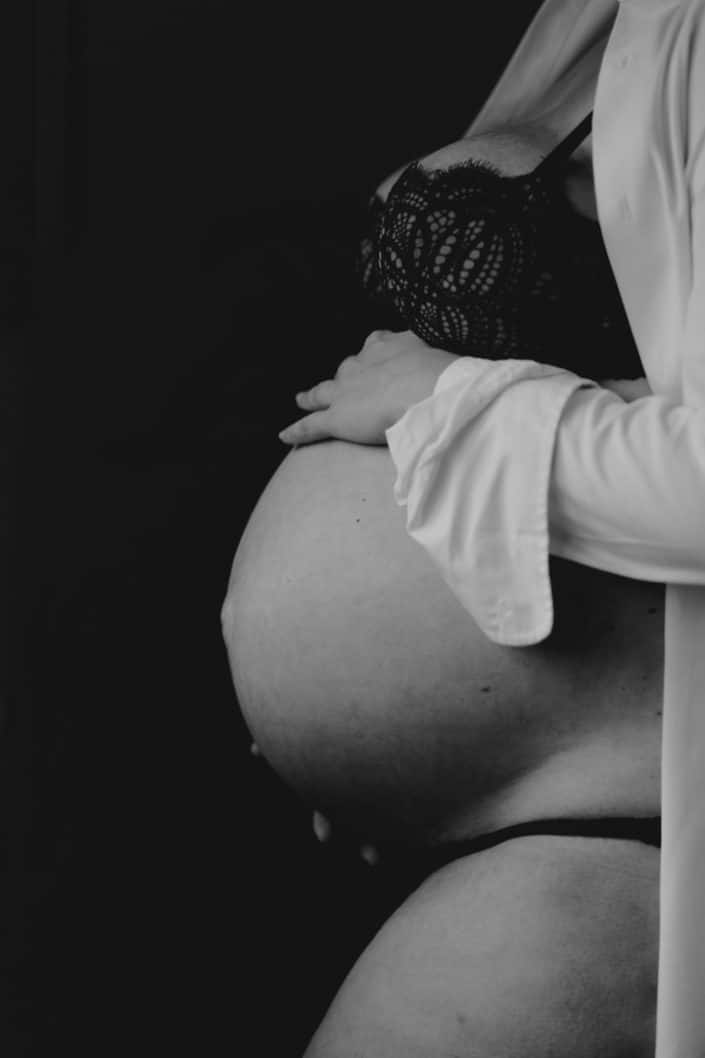 Close up black and white image of baby bump. Mum is wearing white shirt and underwear. Intimate maternity session at home. Hampshire maternity photo shoot. Ewa Jones Photography