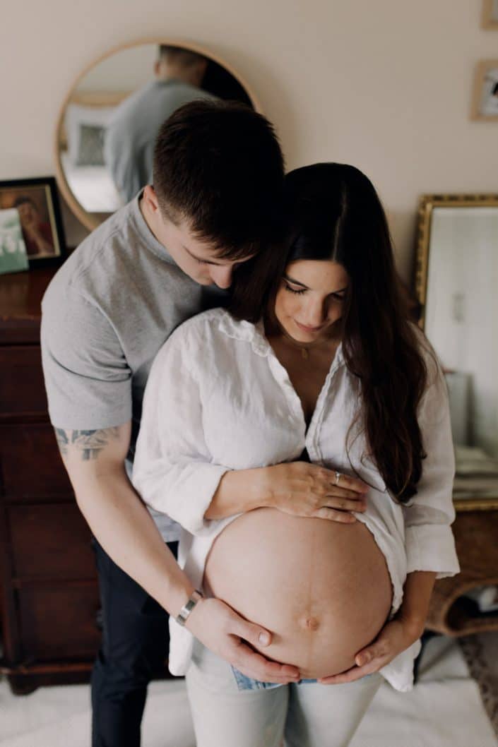 mum and dad are standing and cuddling together. they are touching their baby bump. Maternity photo shoot at home. Hampshire photographer. Ewa Jones Photography