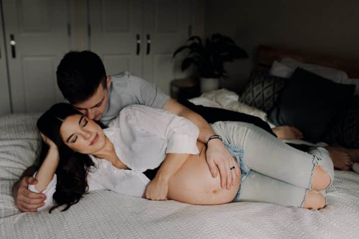 Mum and dad are laying on the bed and being close. dad to be is looking at his wife. maternity photo shoot at home. Hampshire photographer. Ewa Jones Photography