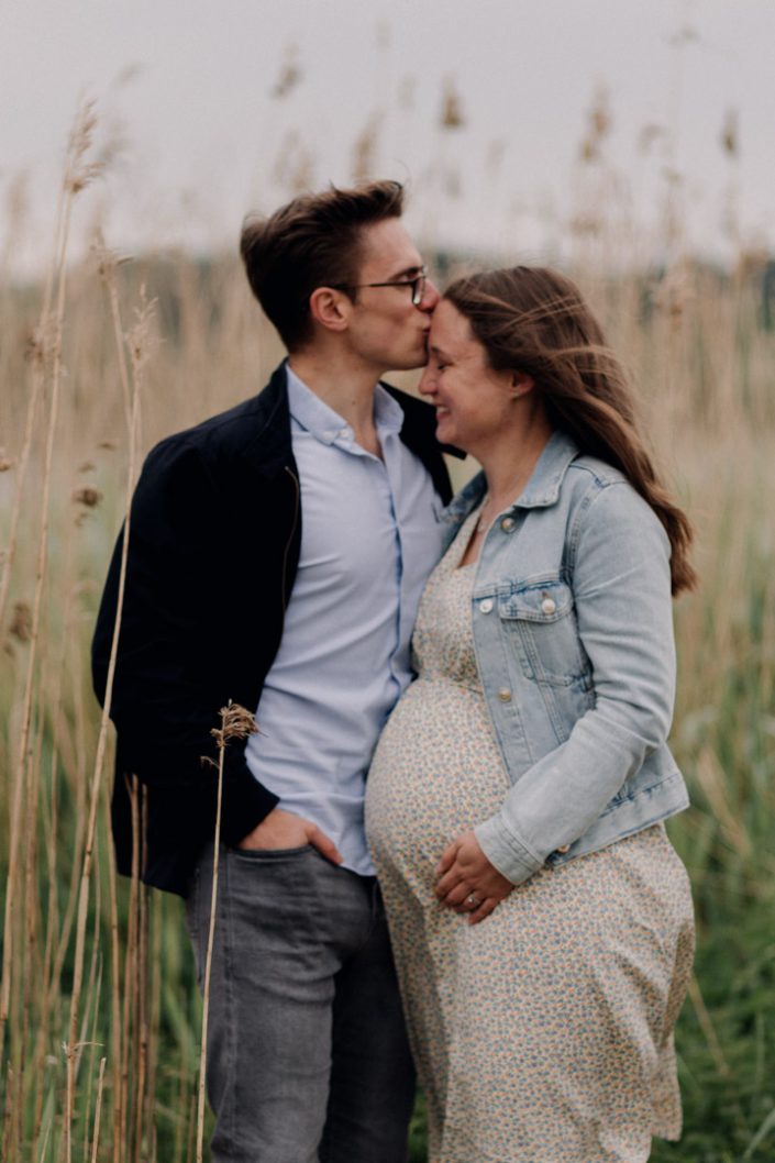 Mum and dad are standing behind the pond and dad is kissing mum. Maternity photo session in Surrey. Surrey maternity photo shoot. Ewa Jones Photography