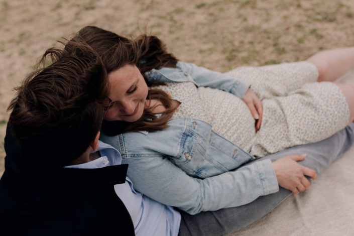 Mum and dad are sitting on the sand and smiling. Maternity photo session in Hampshire. Ewa Jones Photography.