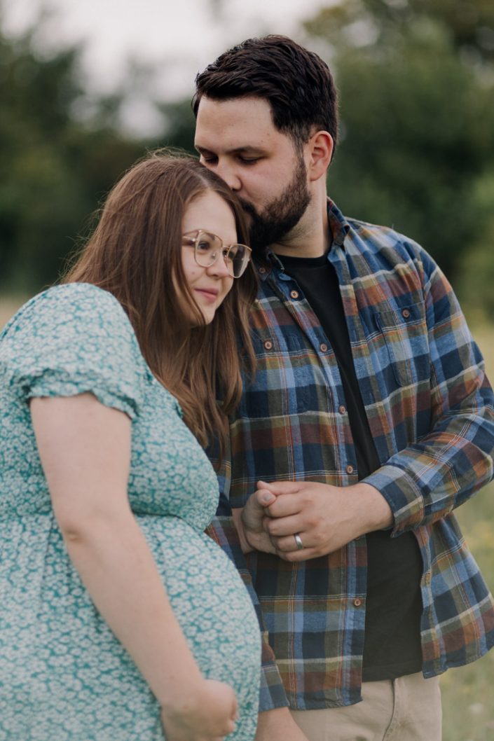 Mum and dad to be are standing in the field and dad is kissing mum. Maternity shoot in Hampshire. Basingstoke photographer. Ewa Jones Photography