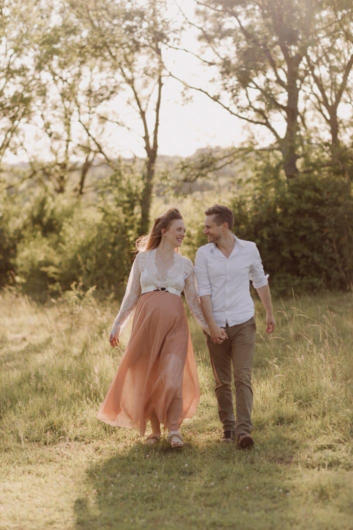 Parents to be are walking in the field and looking at each other. Bump photo session in the fields. What to wear for a maternity session. Basingstoke photographer. Hampshire maternity session. Ewa Jones Photography