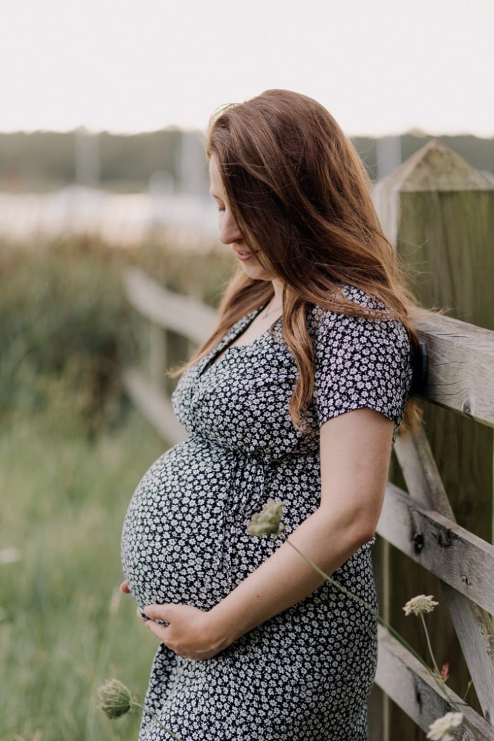 Mum is standing and looking down at the bump. Mum to be is wearing lovely maternity black and white dress. Maternity photo session in Hampshire. Outdoor session. Ewa Jones Photography