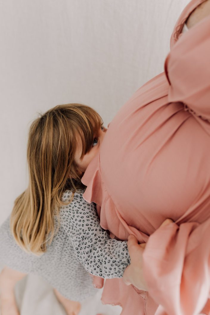 older sister is kissing baby bump. Mum is wearing lovely pink dress. Maternity photo session in Hampshire. Hampshire session. Ewa Jones Photographer