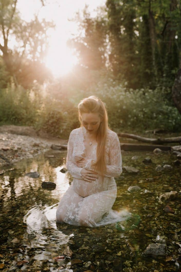 Mother to be is sitting in the river and looking down at her baby. She has a lovely dress. Intimate maternity session. Hampshire photographer. Ewa Jones Photography