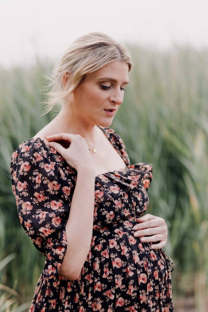 Mum is wearing lovely flowery maternity dress. She is looking down. Maternity session in the Frensham Pond. Surrey maternity photo shoot. Maternity photographer. Ewa Jones Photography