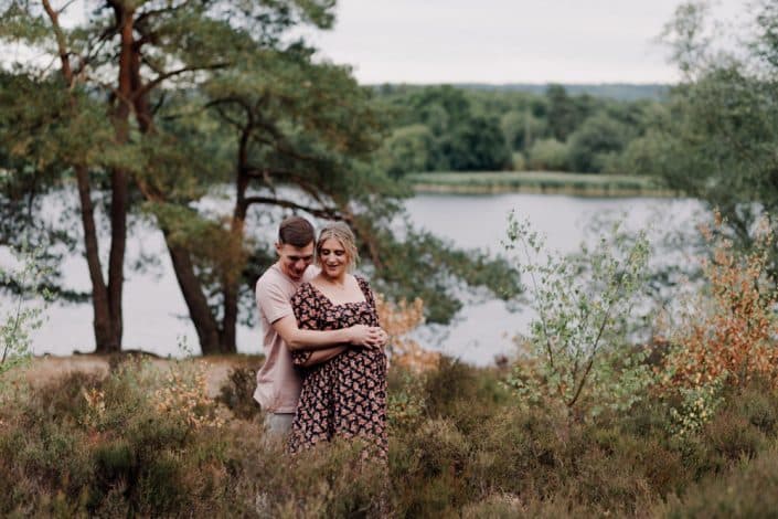 Maternity session at the Frensham Pond. Surrey photographer. Mum to be and dad to be are hugging and looking at baby bump. pond is in the background. Maternity session. Ewa Jones Photography