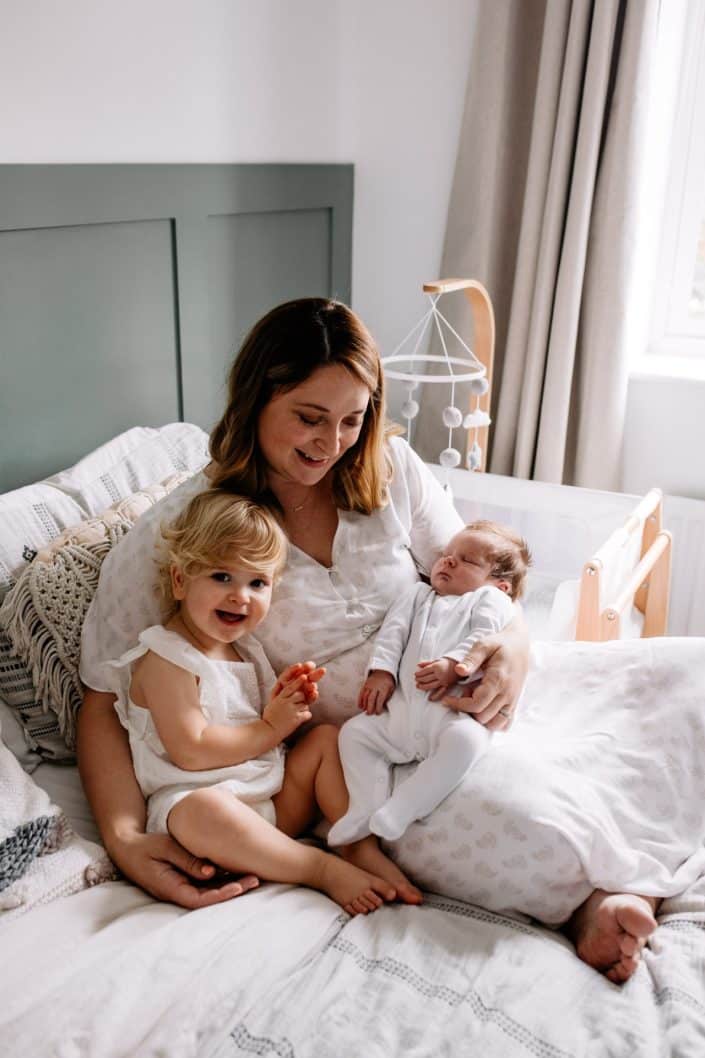 mum is sitting on the bed and cuddling her two children. Lovely natural newborn photo session in Basingstoke. stylish newborn shoot. Basingstoke newborn session. Ewa Jones Photography