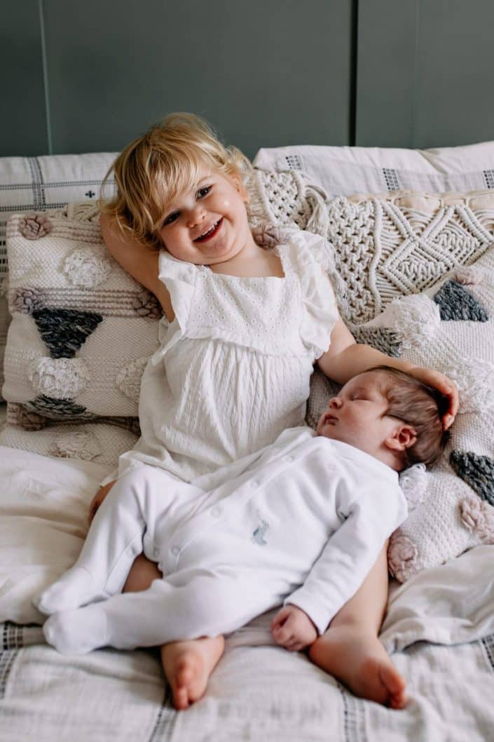 little sister is cuddling baby brother. sister is smiling. in home newborn session in Hampshire. Basingstoke newborn photo shoot. Ewa Jones Photography