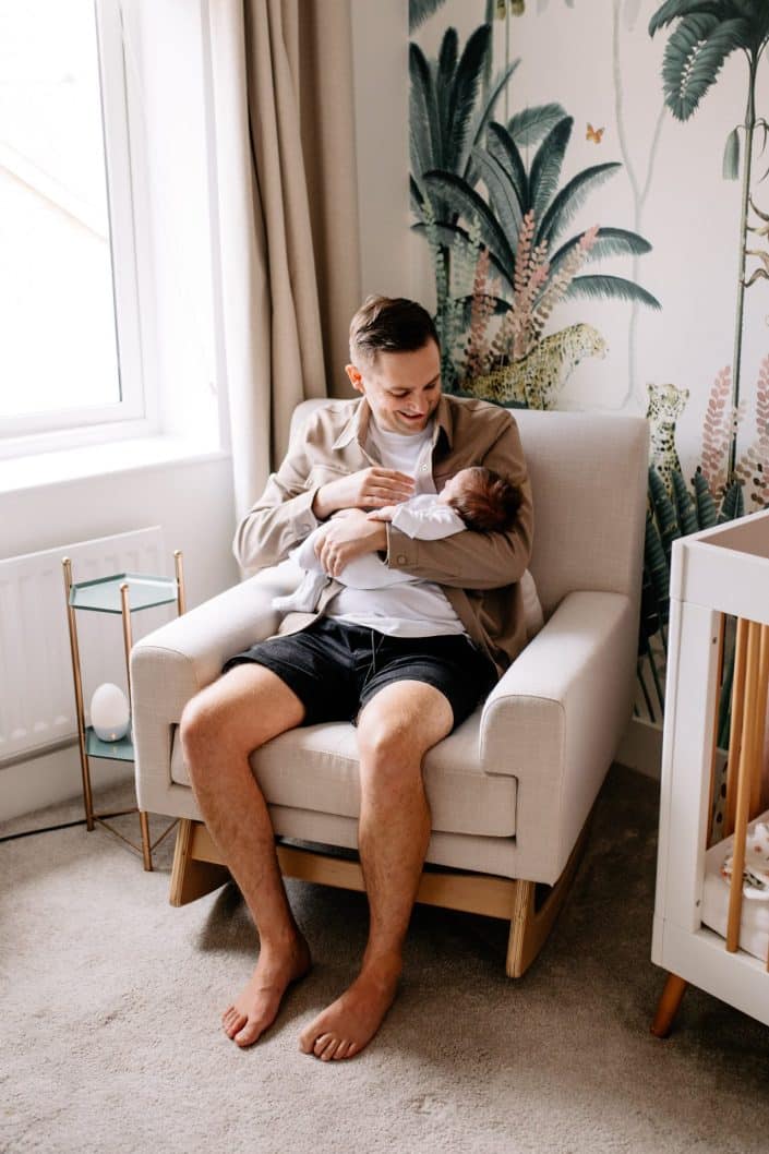 dad is cuddling his newborn baby boy and sitting on the chair in the nursery. newborn shoot in a nice nursery. Basinsgoke photographer. Hampshire newborn photo shoot. Ewa Jones Photography