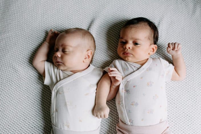 twin newborn baby girls laying on the bed. One baby girl is sleeping and one has eyes open. In home natural newborn photo session. Hampshire photographer. Ewa Jones Photography