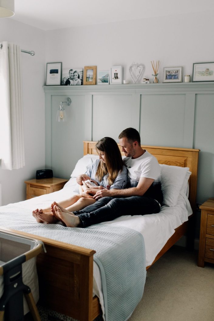 mum and dad are cuddling their baby boy close. they are sitting on the bed. Hampshire newborn session at home. Ewa Jones Photography