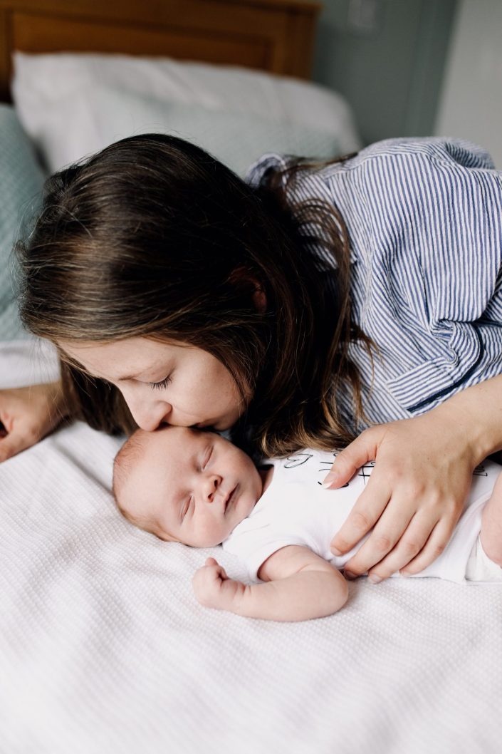 mum is kissing her newborn baby. baby is laying on the bed sleeping. In home natural intimate photo session. Ewa Jones Photography