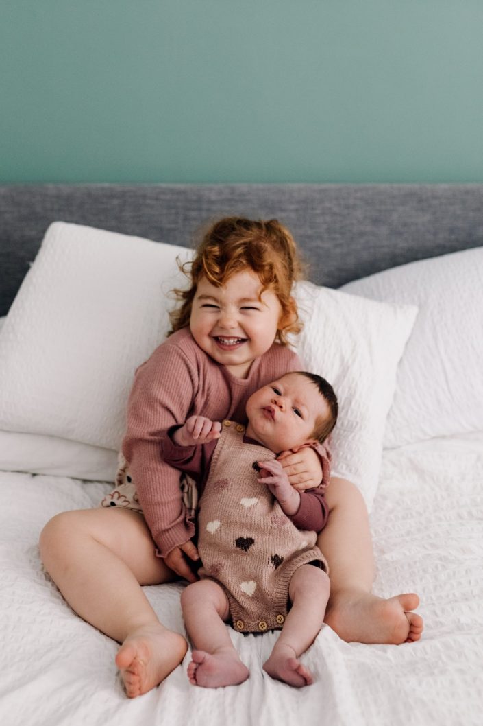 big sister is cuddling baby sister. big sister is smiling. lovely natural photo shoot at home. Hampshire photo session. Ewa Jones Photography