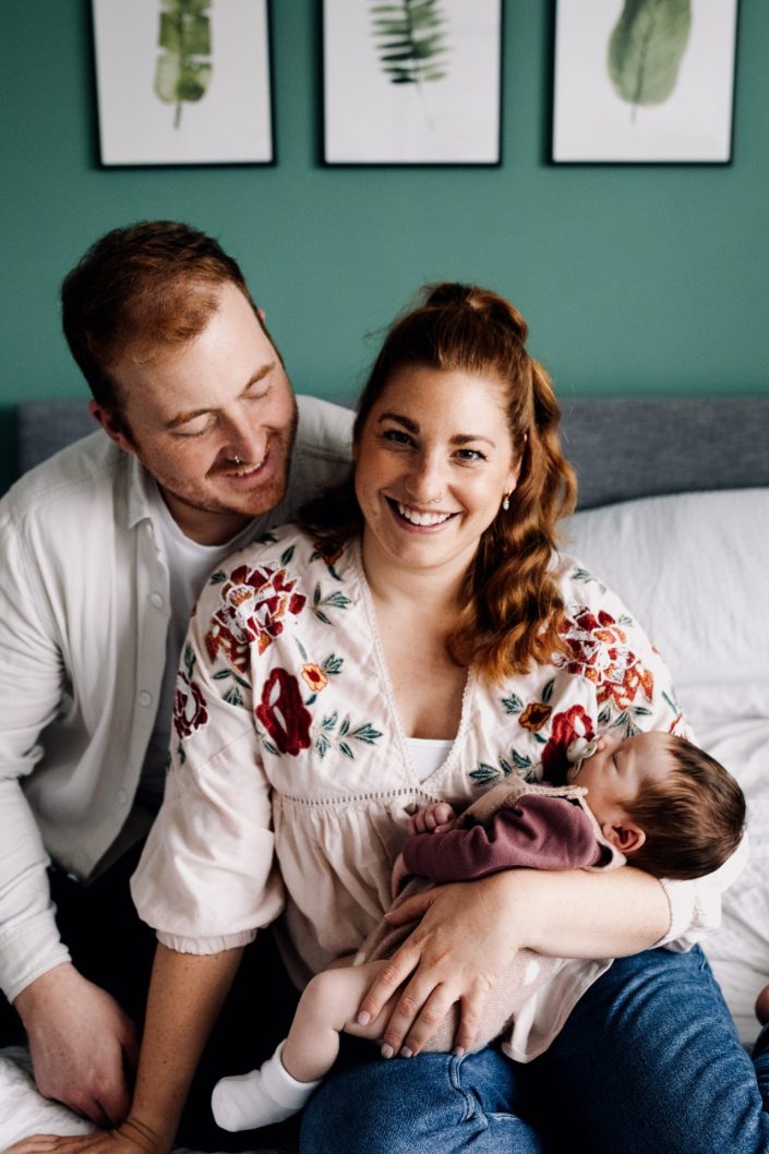 mum and dad are on the bed cuddling their baby girl. Newborn session at home. Basingstoke newborn photographer. Ewa Jones Photography