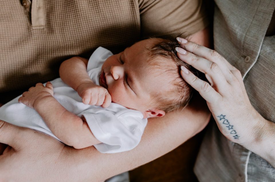 baby is wearing white baby grow. mum is putting her hand on the babies head. Hampshire newborn photo shoot. Ewa Jones Photography